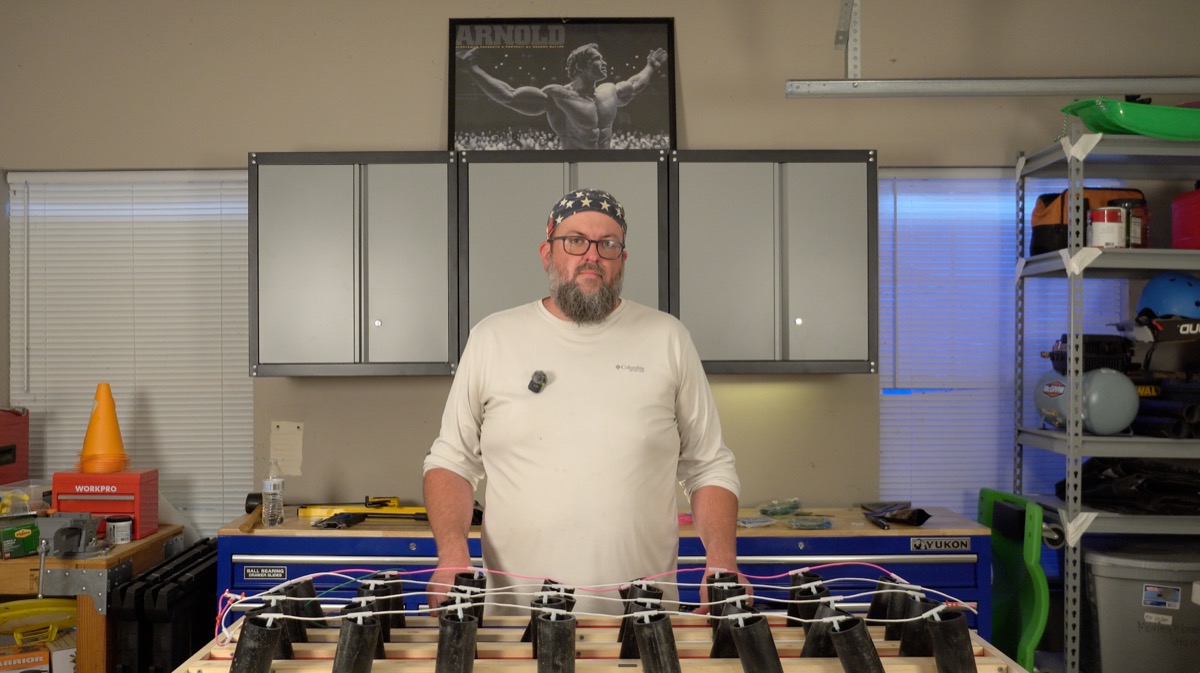 Builder standing behind a finished mortar rack with quick-match fuse wired across all tubes
